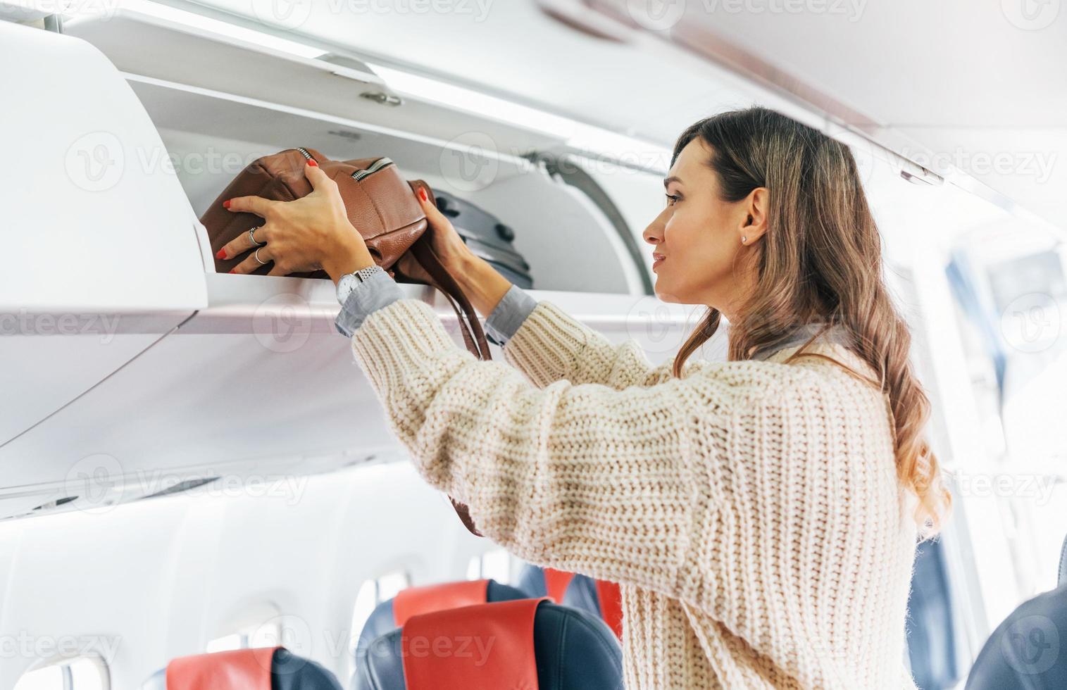 Gepäck halten. junge weibliche passagierin in lässiger kleidung ist im flugzeug foto