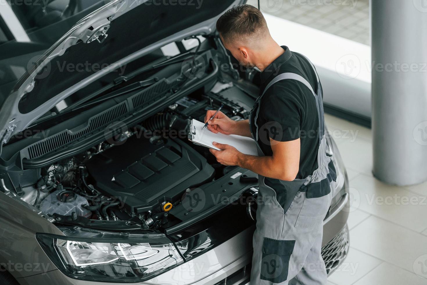 Motor Reparatur. Mann in Uniform arbeitet tagsüber im Autosalon foto