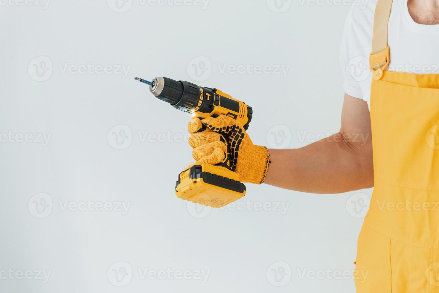 heimwerker in gelber uniform, der mit automatischem schraubendreher gegen weiße wand steht. haussanierungskonzept foto