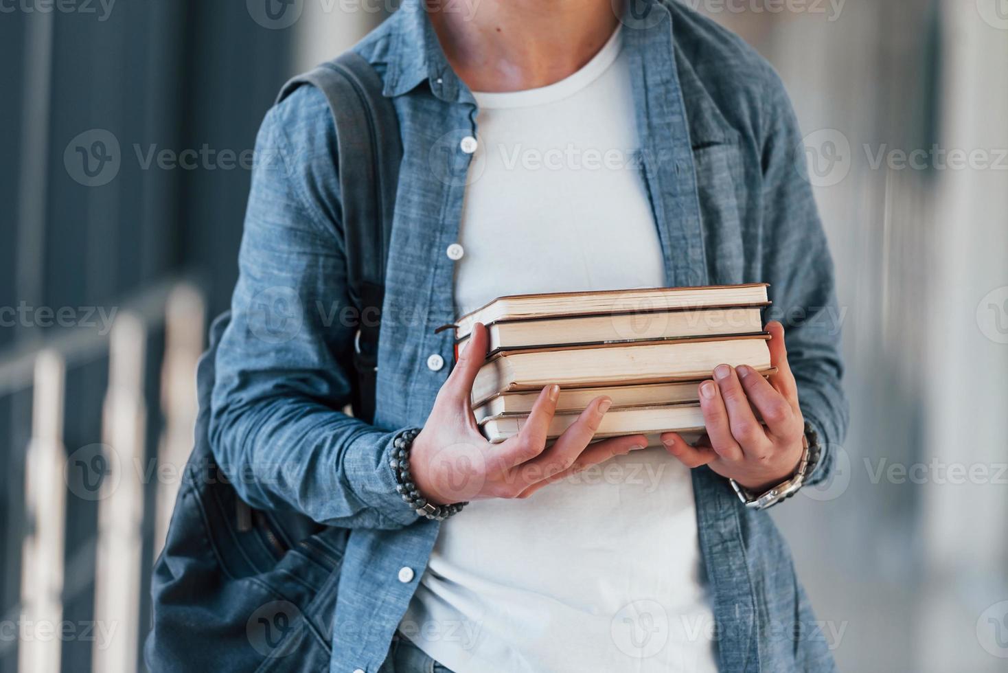 Nahaufnahme eines jungen Studenten in Jeanskleidung, der sich mit Büchern in den Händen im Korridor eines Colleges befindet foto