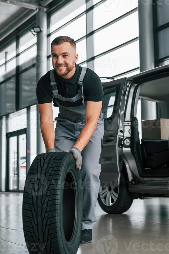 nagelneuer Reifen. Mann in Uniform arbeitet tagsüber im Autosalon foto