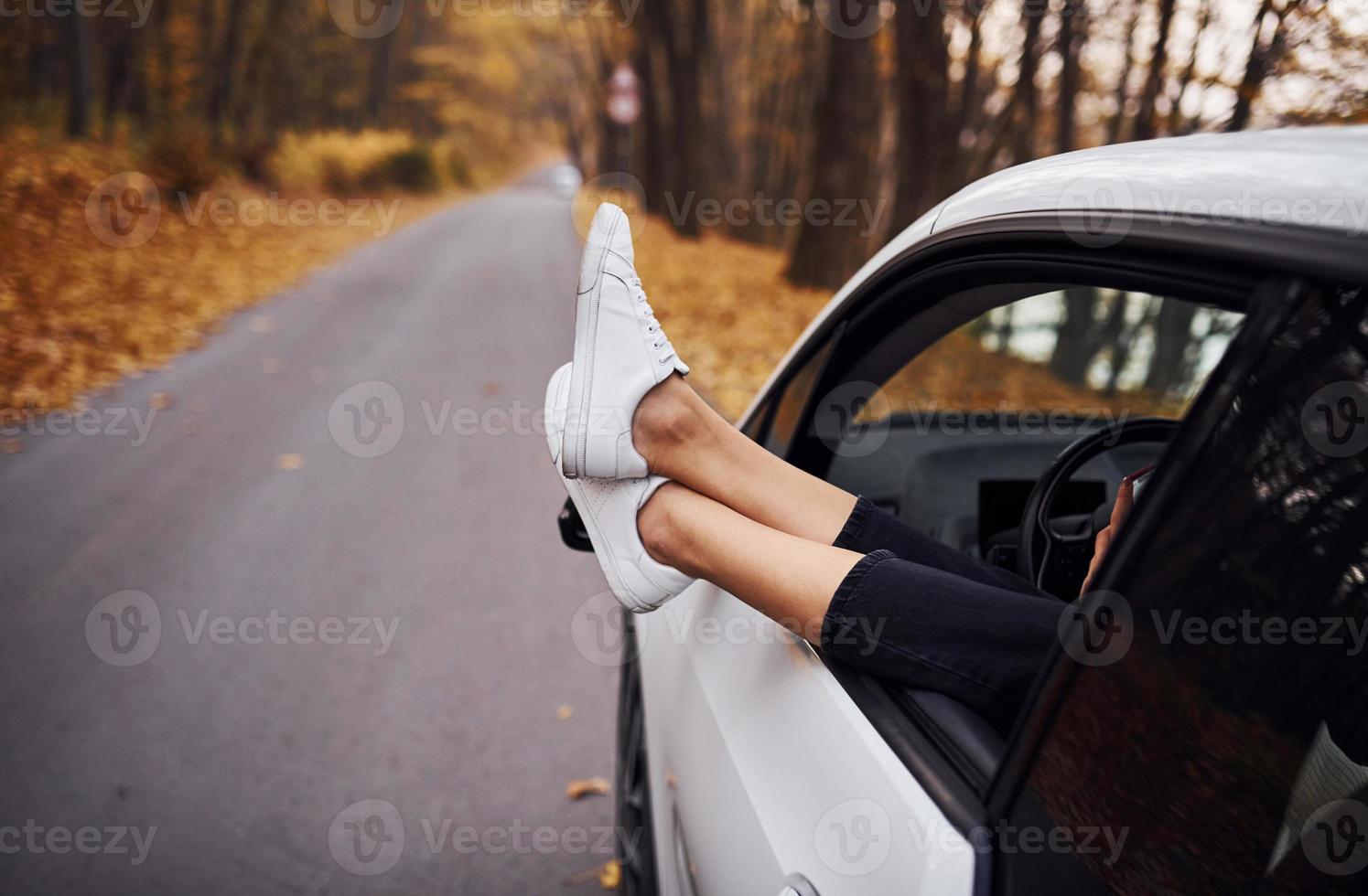 Frauenbeine sind aus dem Autofenster. modernes, brandneues Auto im Wald foto