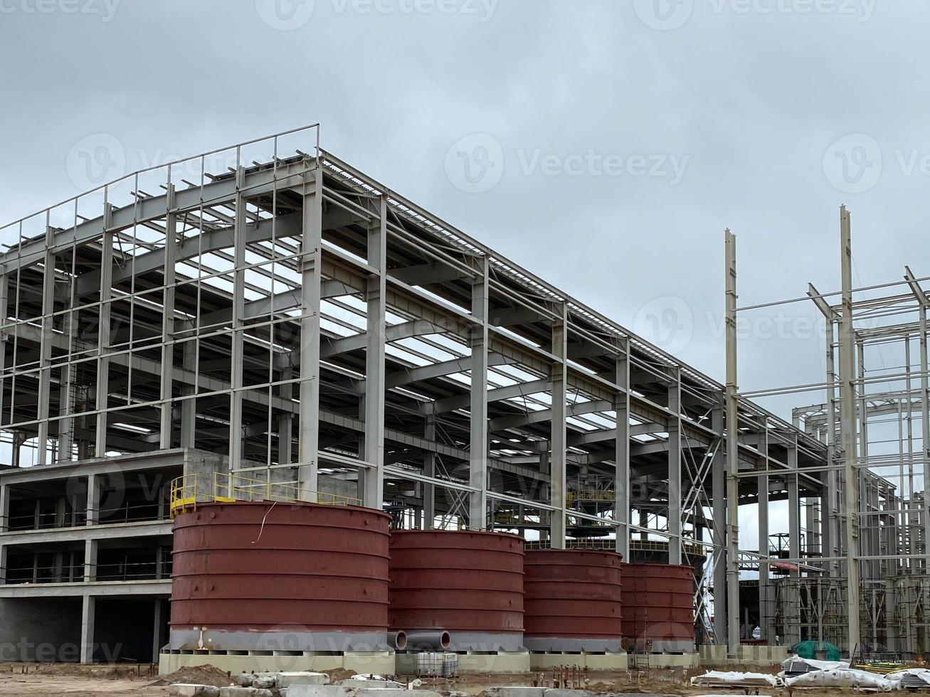 Stahlkonstruktion des neuen Industriegebäudes unter wolkenblauem Himmel. Strukturrahmenbalken der neuen Technologie der Fabrik im Bau. Rohstahlrahmenhersteller und Teleskopkran, Sand, Kies foto