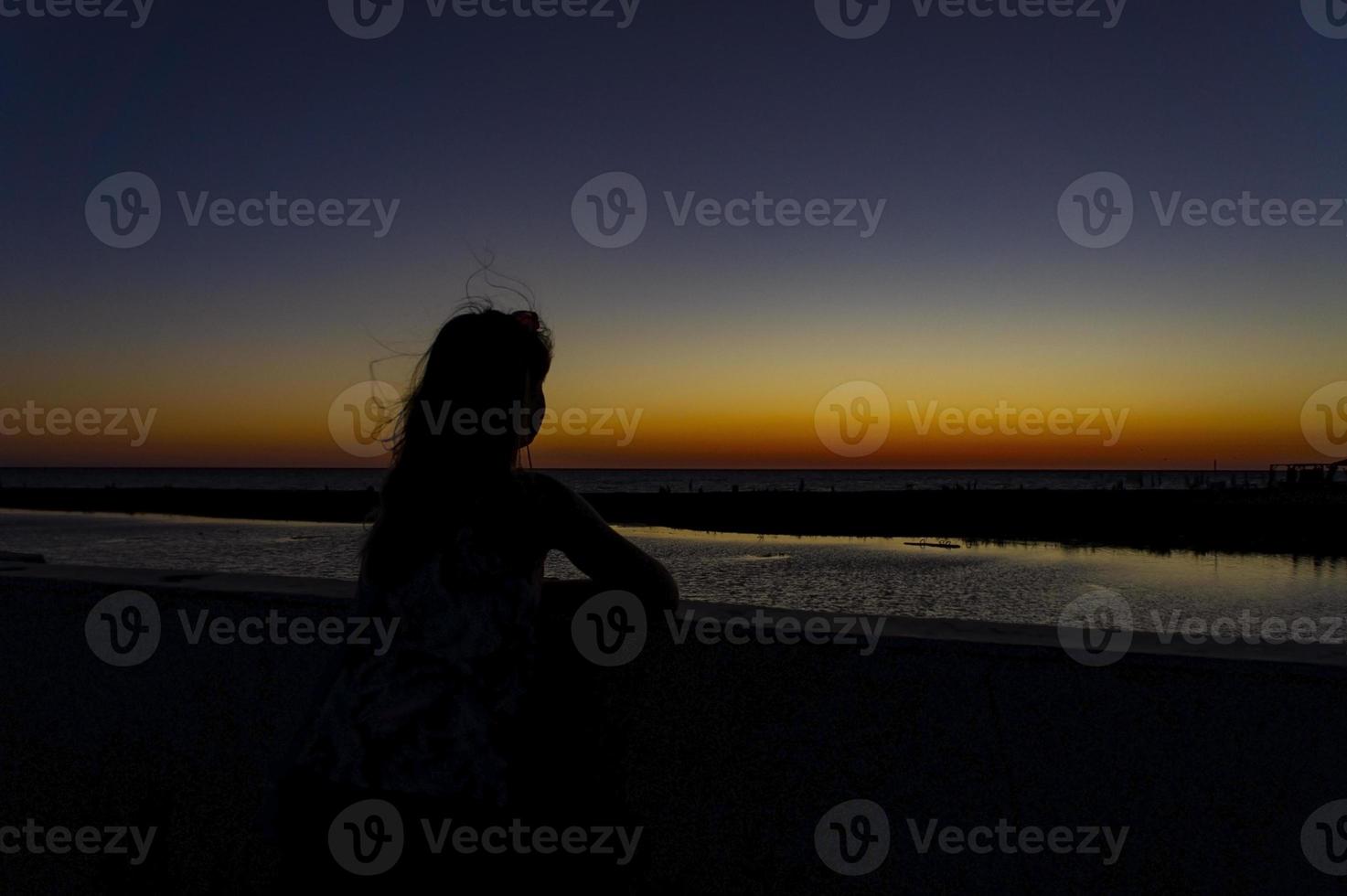 Silhouette einer jungen Frau mit flatterndem Haar vor dem Hintergrund eines hellen Sonnenuntergangs foto