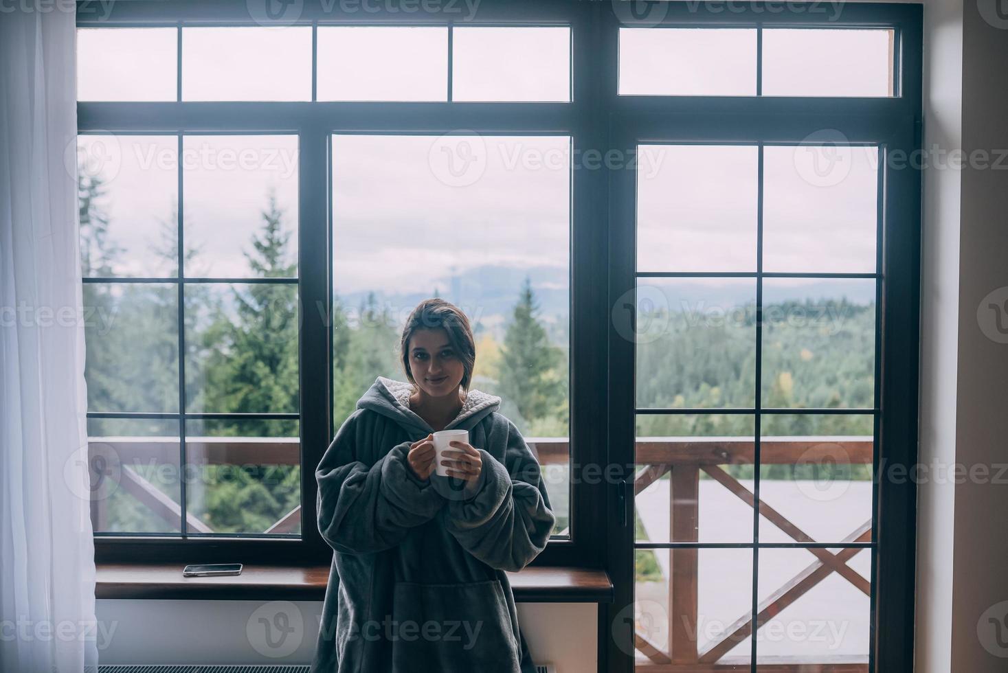 junge frau, die am fenster steht, hält einen becher foto