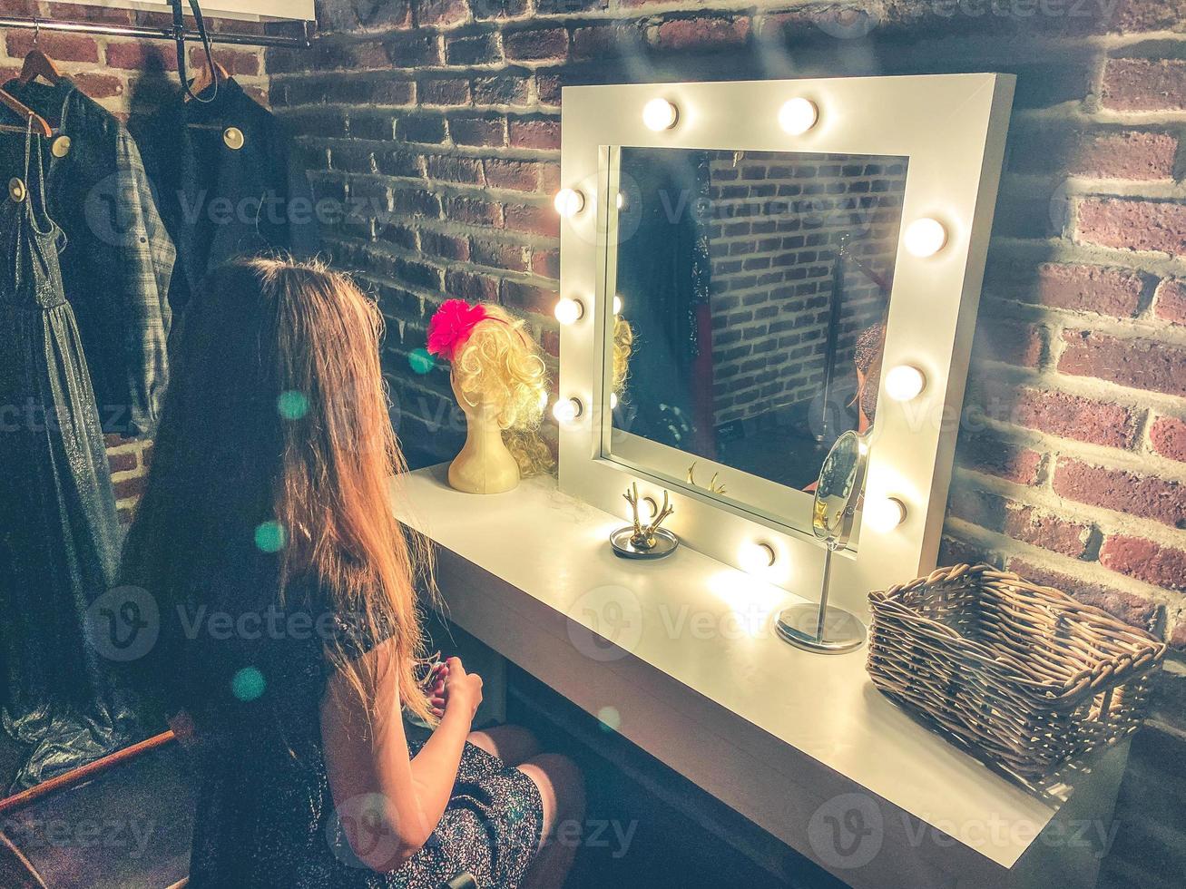 ein Ankleidezimmer, ein großer Spiegel mit Glühbirnen, in dem ein Mädchen in einem Kleid mit langen Haaren sitzt. frau schminkt sich und macht sich fertig zum ausgehen foto