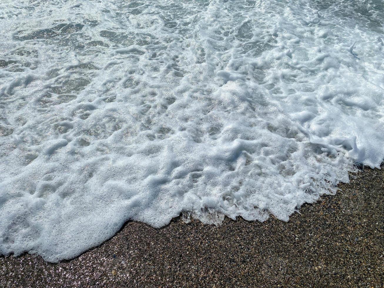 Wasserwellen im Meer und Sand mit kleinen natürlichen bunten Steinen an der Küste, kleine Kieselsteine am Strand. Hintergrund, Textur foto