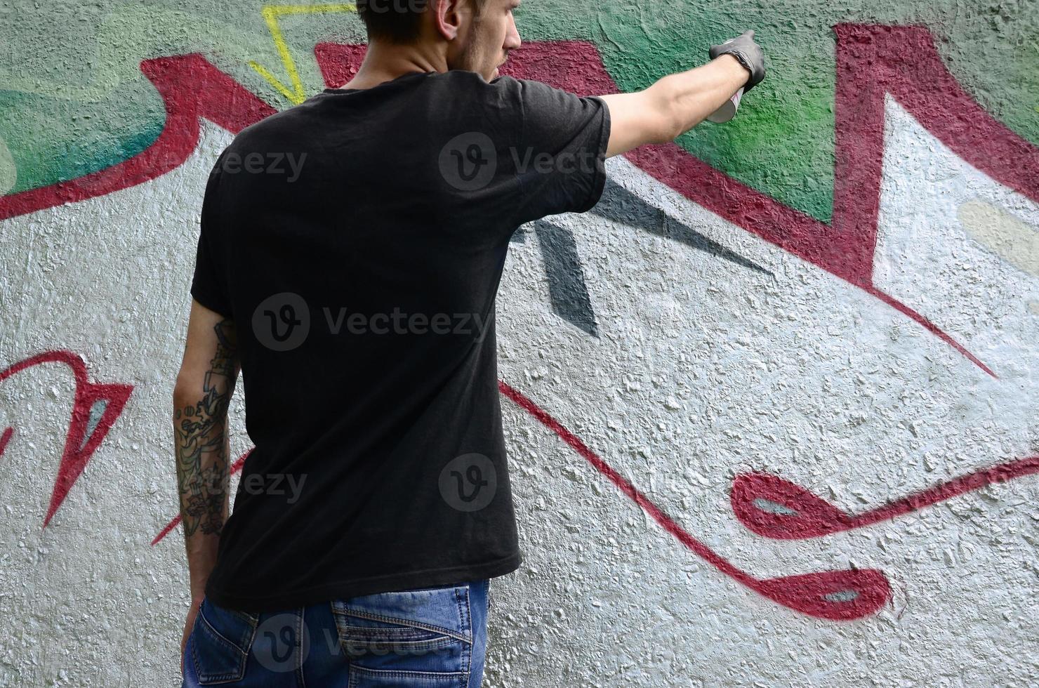 Ein junger Hooligan malt Graffiti auf eine Betonwand. illegales vandalismuskonzept. Straßenkunst foto