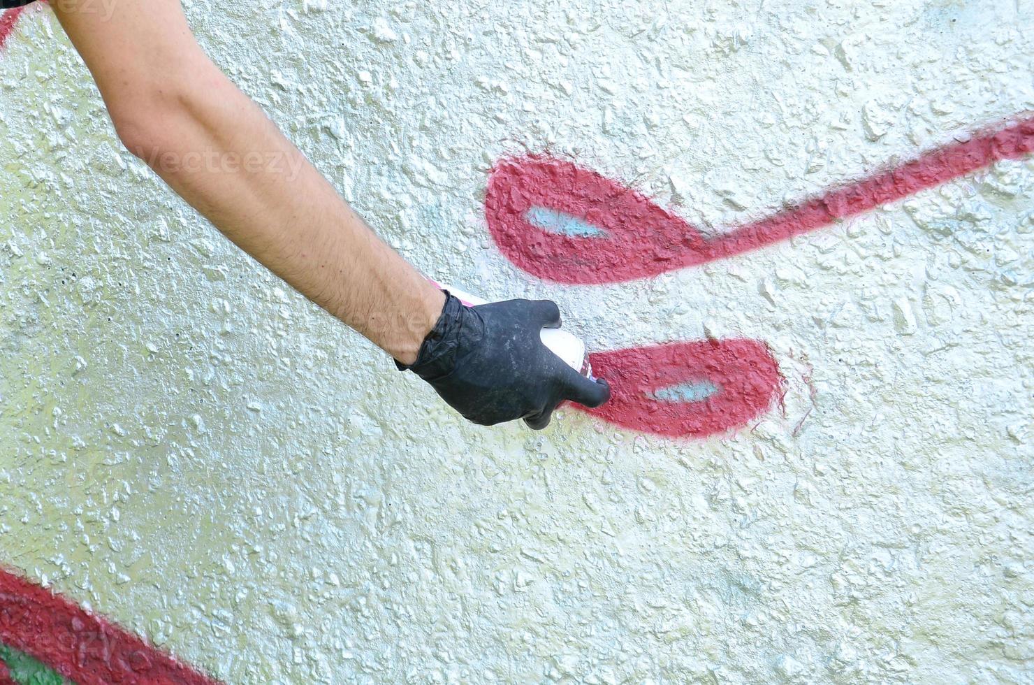 Eine Hand in schwarzen Handschuhen malt Graffiti auf eine Betonwand. illegales vandalismuskonzept. Straßenkunst foto