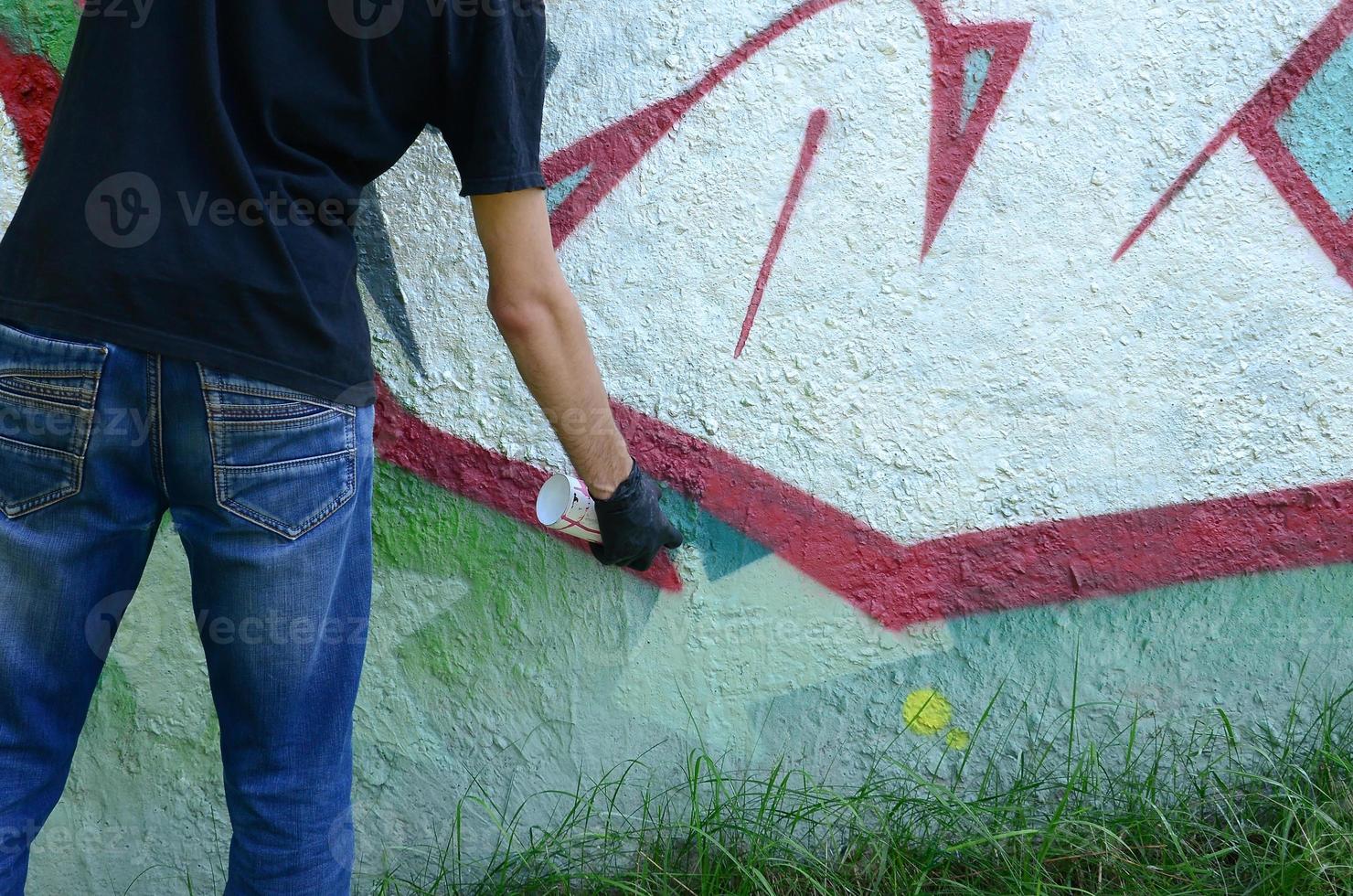 Ein junger Hooligan malt Graffiti auf eine Betonwand. illegales vandalismuskonzept. Straßenkunst foto