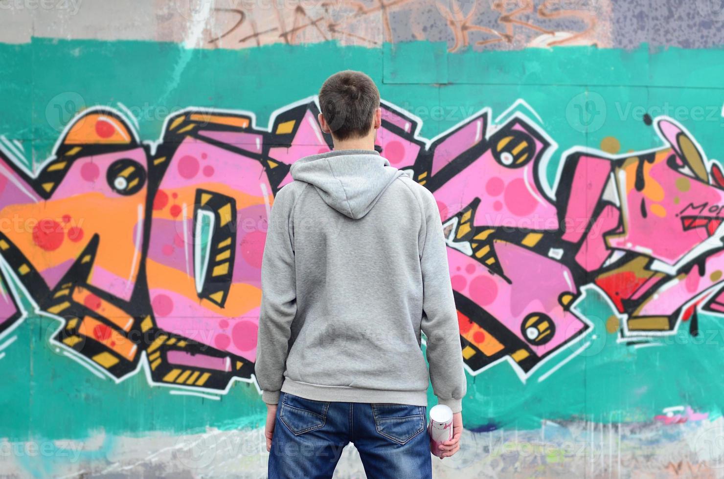 Ein junger Graffiti-Künstler in einem grauen Hoodie blickt mit auf die Wand foto