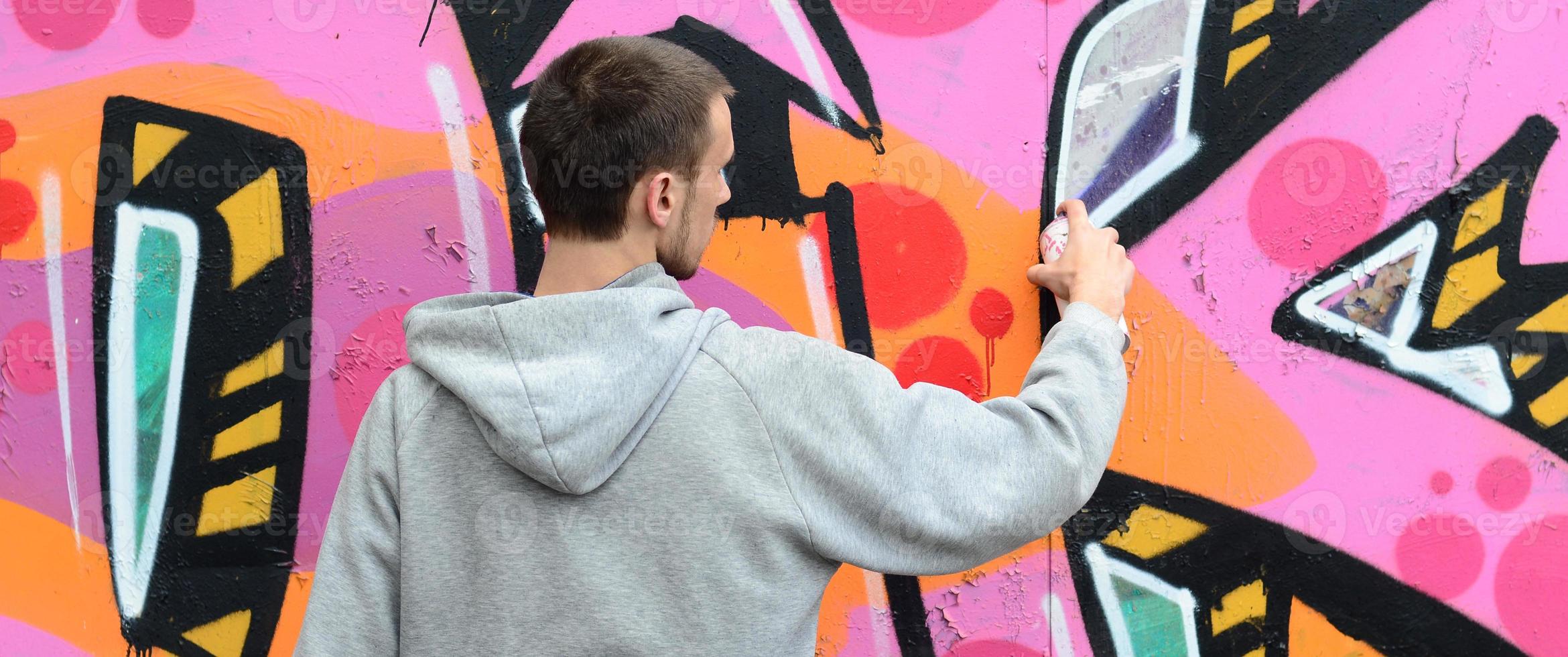 ein junger Mann in einem grauen Hoodie malt Graffiti in Pink und Grün c foto