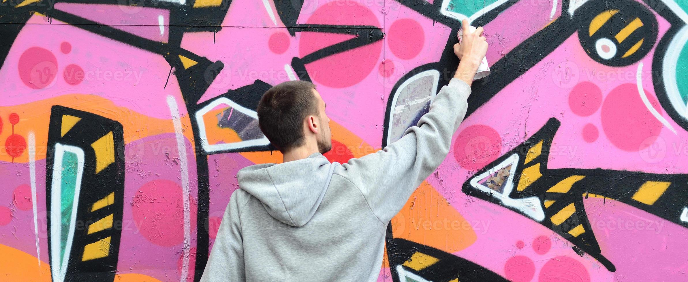 ein junger Mann in einem grauen Hoodie malt Graffiti in Pink und Grün c foto