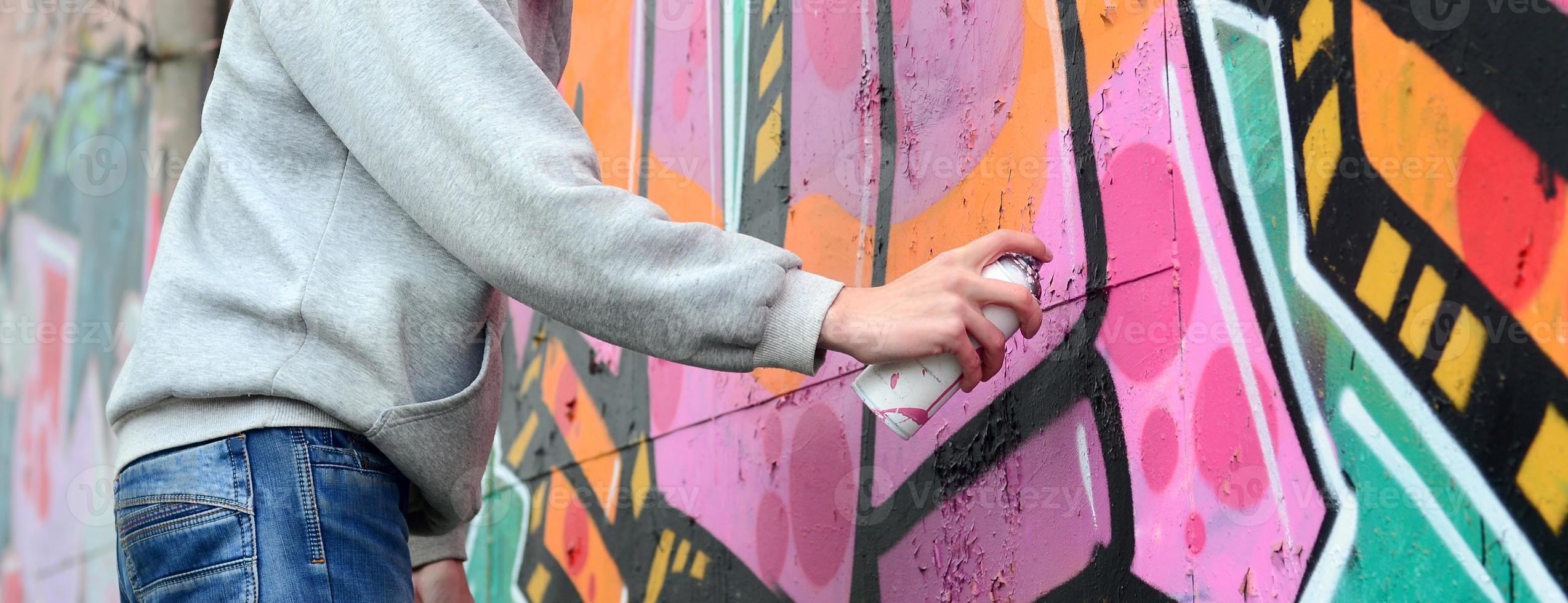 Die Hand eines jungen Mannes in einem grauen Hoodie malt Graffiti in Pink und foto