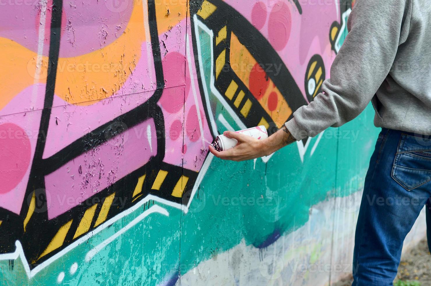 Die Hand eines jungen Mannes in einem grauen Hoodie malt Graffiti in Pink und foto