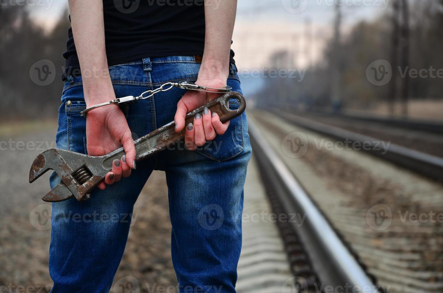 das Mädchen in Handschellen mit dem verstellbaren Schraubenschlüssel auf der Eisenbahn foto