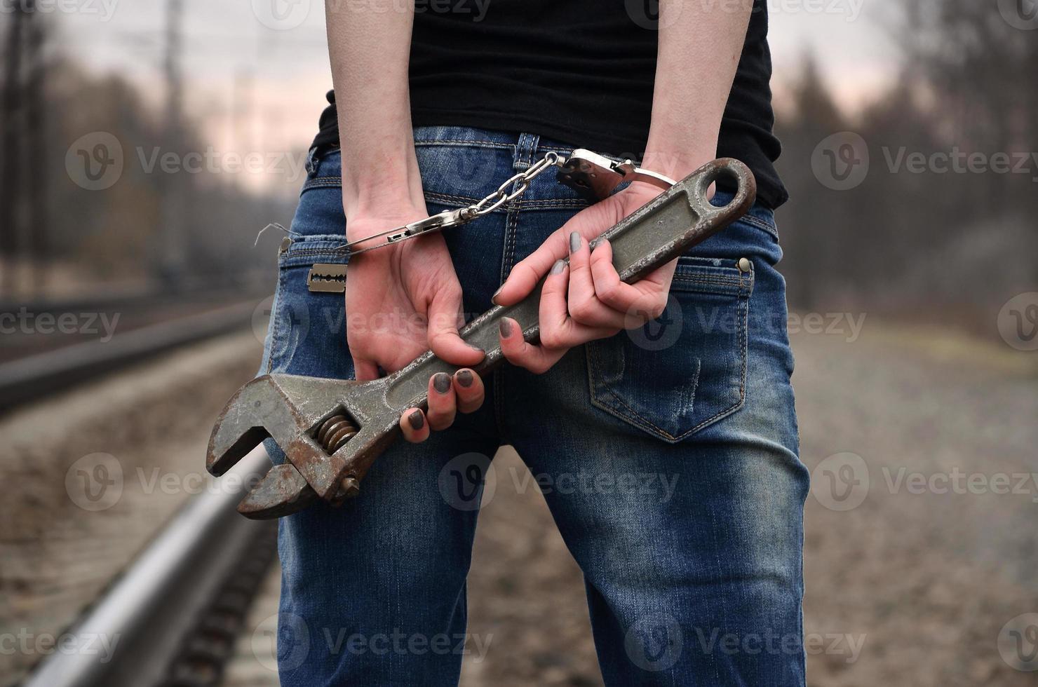 das Mädchen in Handschellen mit dem verstellbaren Schraubenschlüssel auf dem Gleishintergrund. das Konzept der Kriminalprävention unter Beteiligung von Bahn und Zügen. foto