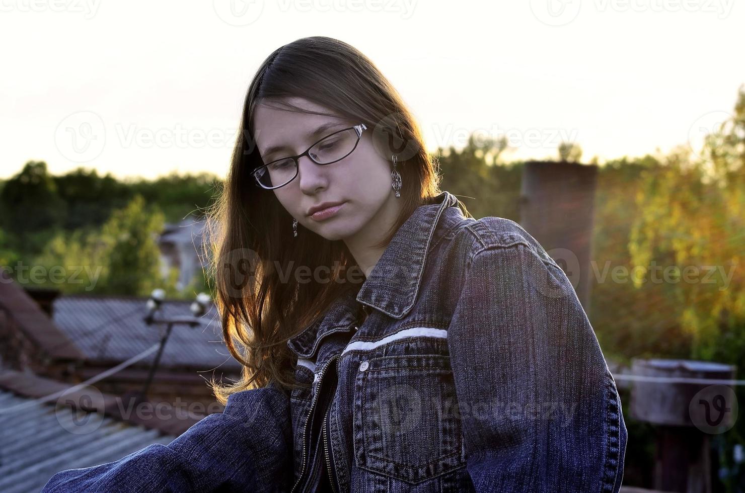 Mädchen in Brille und Jeansjacke ruht auf dem Dach eines Hauses foto