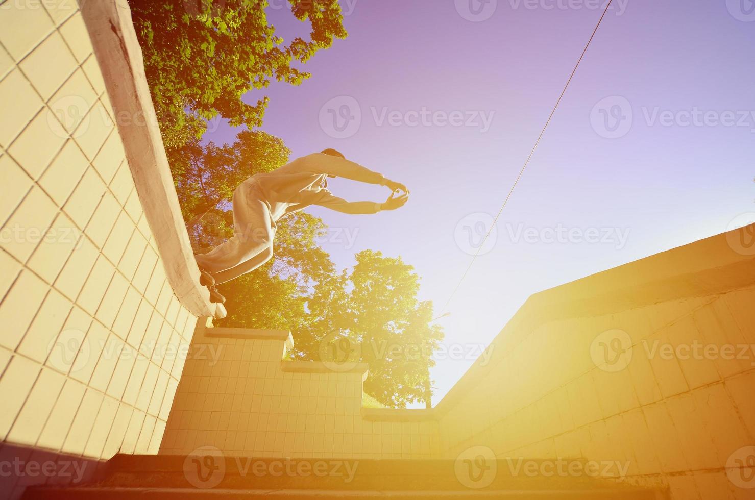 ein junger mann macht einen sprung durch den raum zwischen den betonbrüstungen. Der Athlet übt Parkour und trainiert unter Straßenbedingungen. Untersicht foto