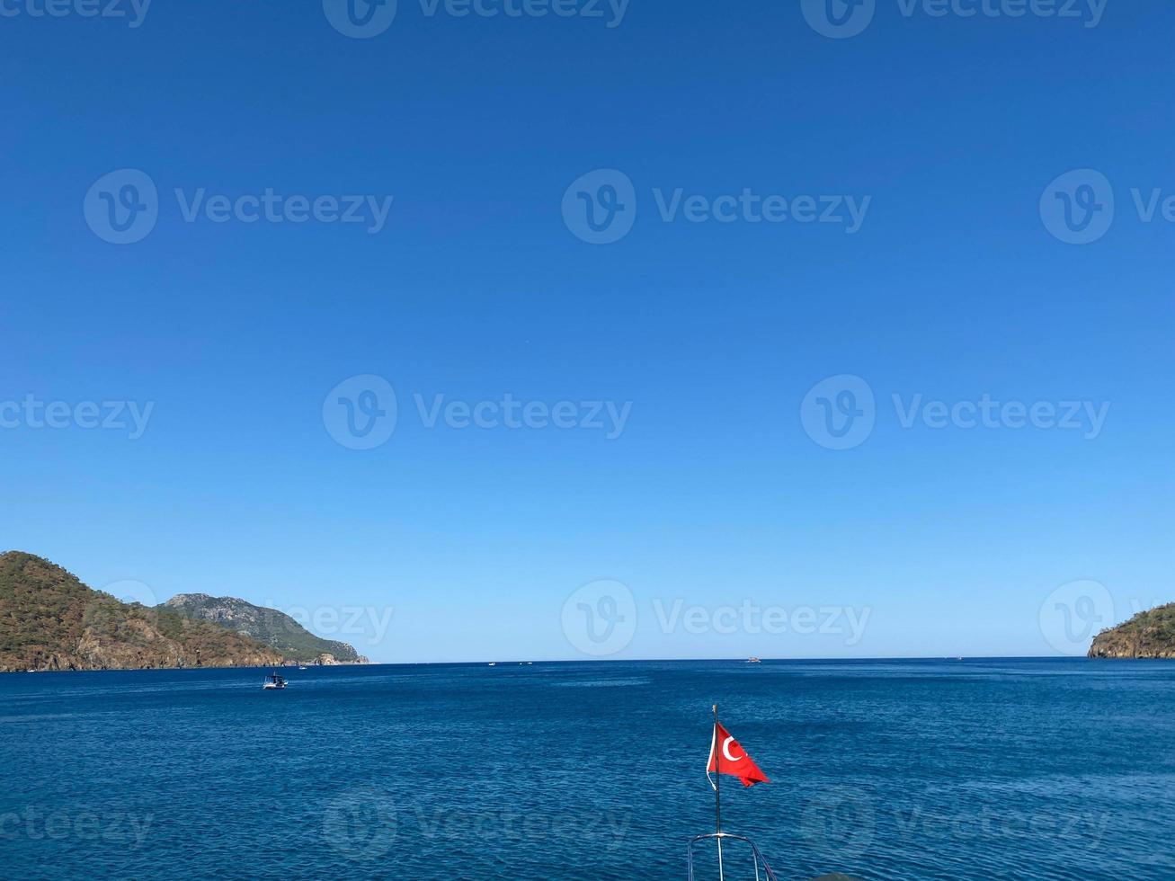 die schwenkende türkische flagge auf einem ruhigen seehintergrund mit einem boot und einem blauen himmel foto