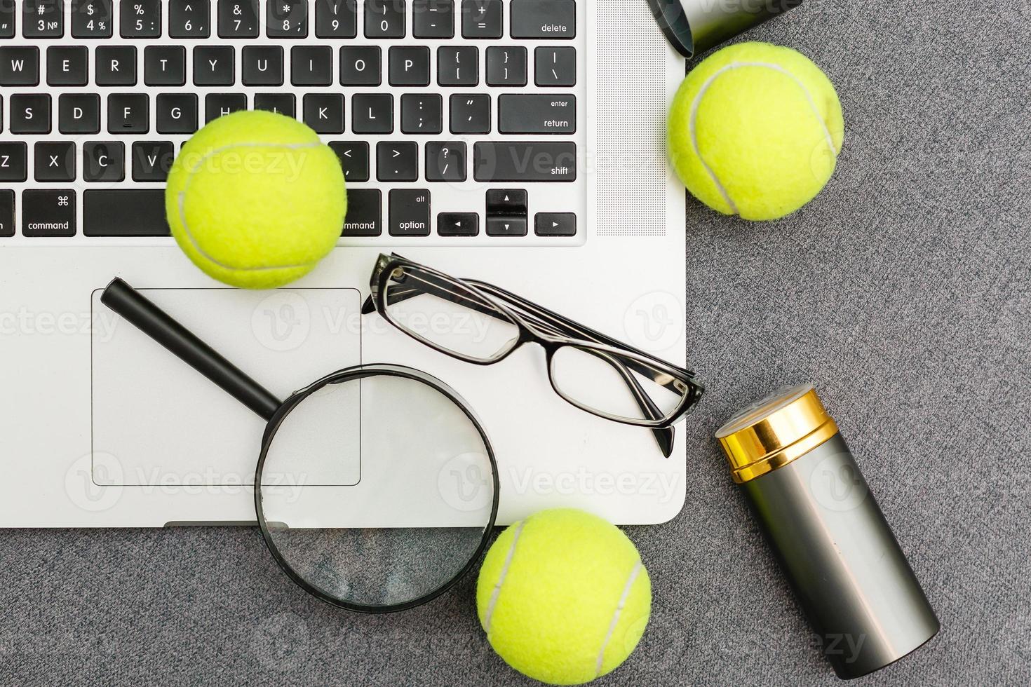 draufsicht auf laptop, sportgeräte, tennisball, federball, brille auf dem grauen tisch der sportverwaltung. geschäftskonzept. foto