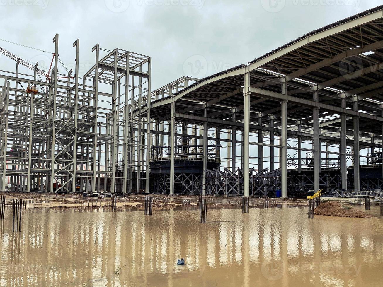 Bau eines neuen Komplexes im Werk. Metallkonstruktionen für den Bau des Fundaments. Baumaterial ist mit Rost bedeckt und liegt in einer Wasserpfütze foto