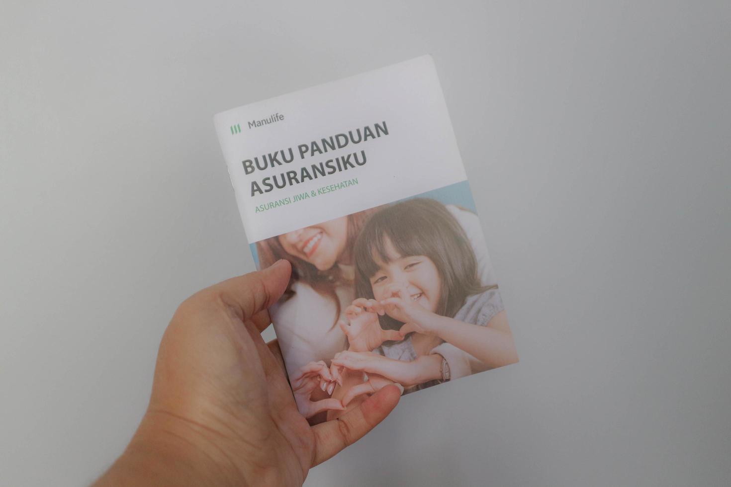 west java, indonesien im juli 2022. eine hand, die manulife's versicherungshandbuch für lebens- und krankenversicherungen hält foto