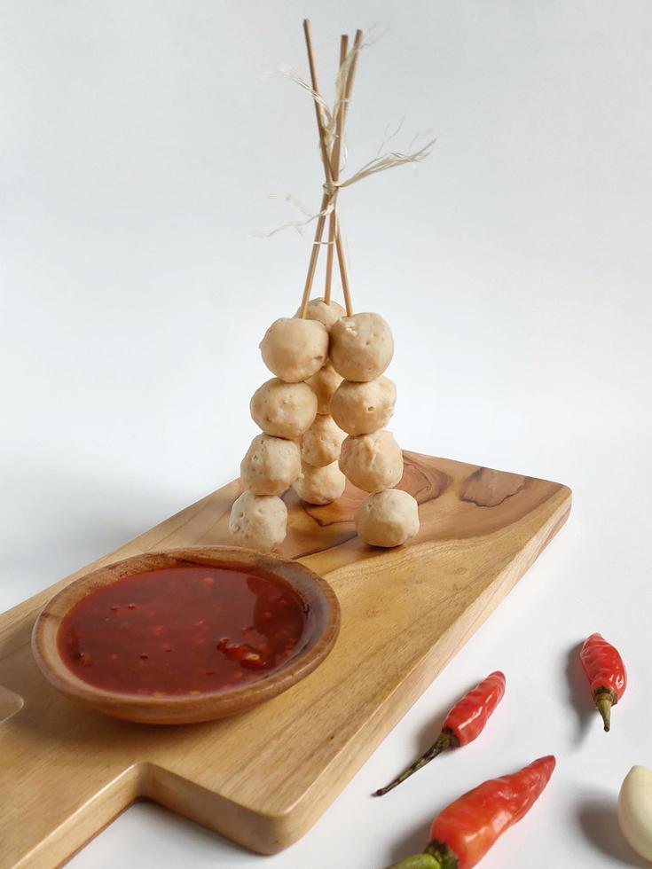 Auf dem Holzbrett stehende, aufgespießte Fleischbällchen mit scharfer Soße, garniert mit rotem Chili und Knoblauch foto