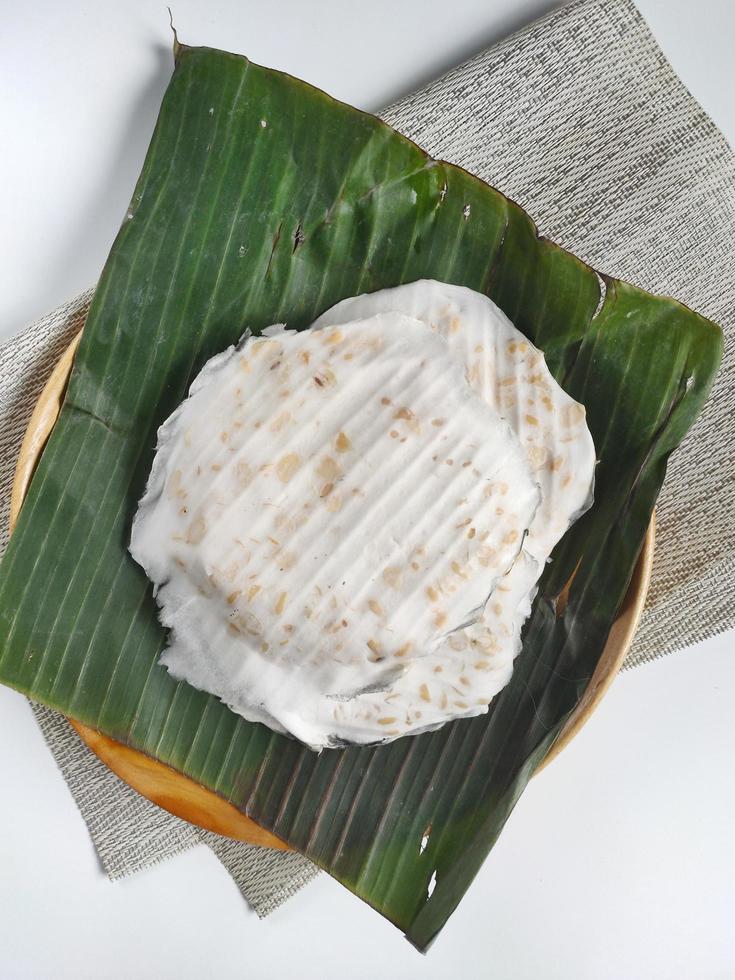 Tempeh mendoan platziert auf Bananenblatt und Holzplatte mit weißem Hintergrund. Tempeh Mendoan ist eine in Indonesien beliebte Art von Tempeh. es ist flach, dünn und breit. Es wird in Bananenblättern fermentiert foto