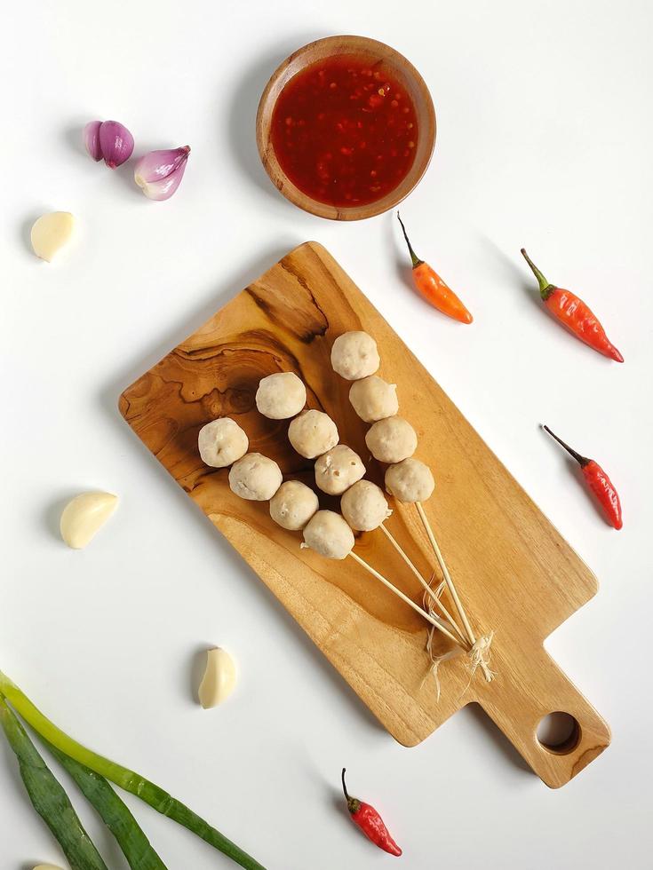 aufgespießte Fleischbällchen mit würziger Sauce auf dem Holzschneidebrett, garniert mit Knoblauch, Schalotten, roten Chilis und Lauch foto