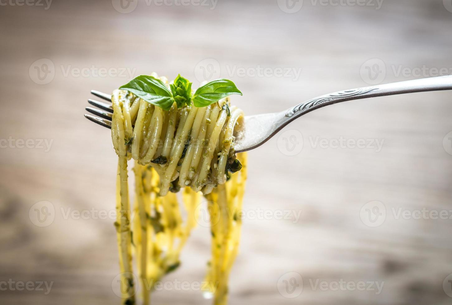 Spaghetti mit Pesto-Sauce und Basilikumblatt auf der Gabel foto