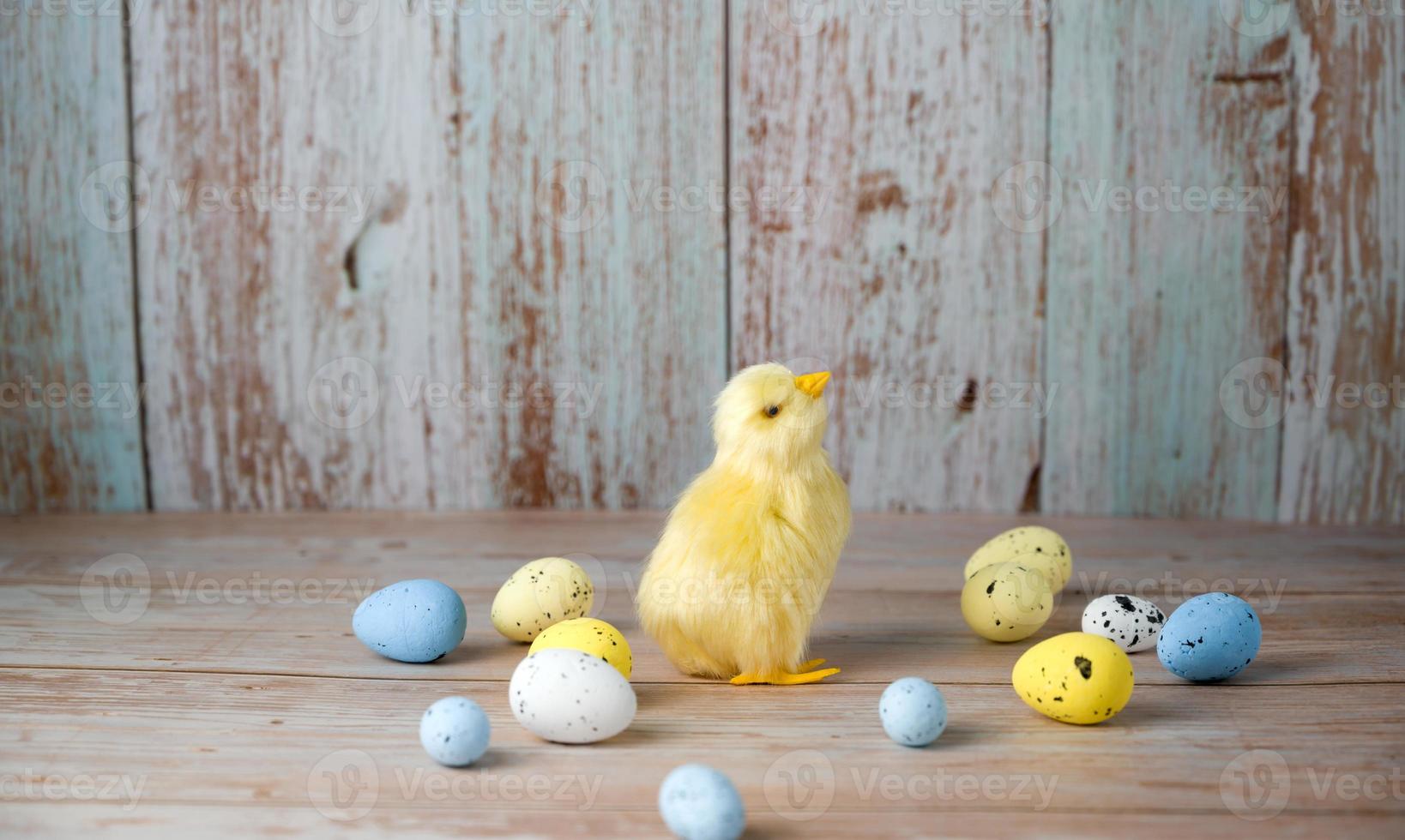 Ostergrußkarte mit kleinem Huhn, umgeben von bunten Eiern vor blauem Hintergrund foto