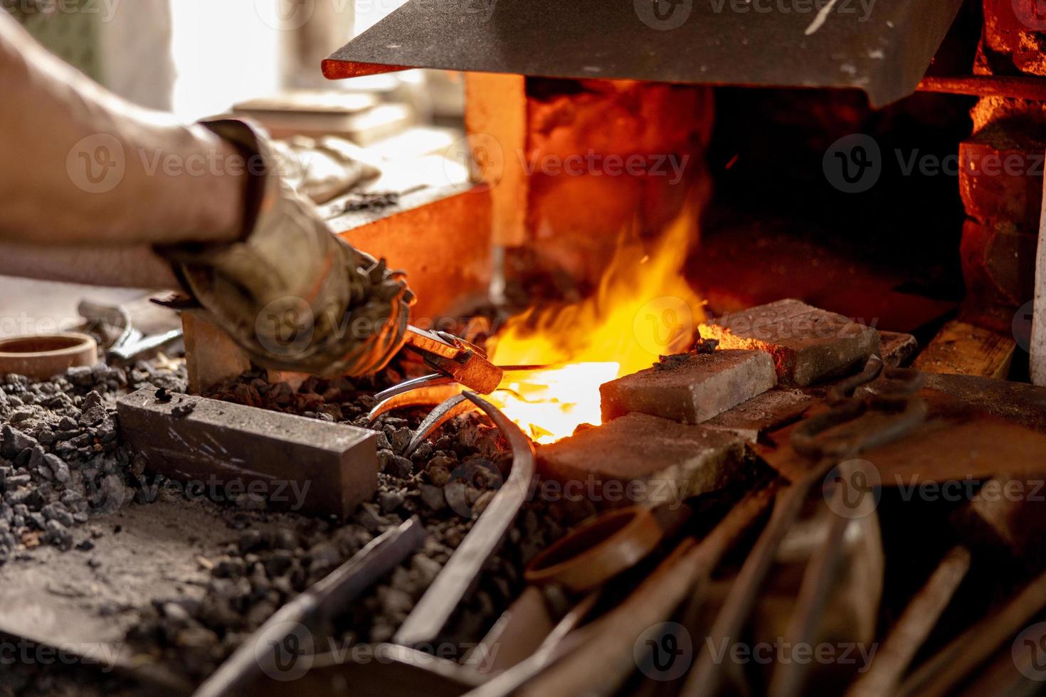 der Schmied im Produktionsprozess von Metallprodukten, handgefertigt in der Schmiede. Handwerker erhitzt Metall im Feuer. Metallindustrie, alter Beruf. foto