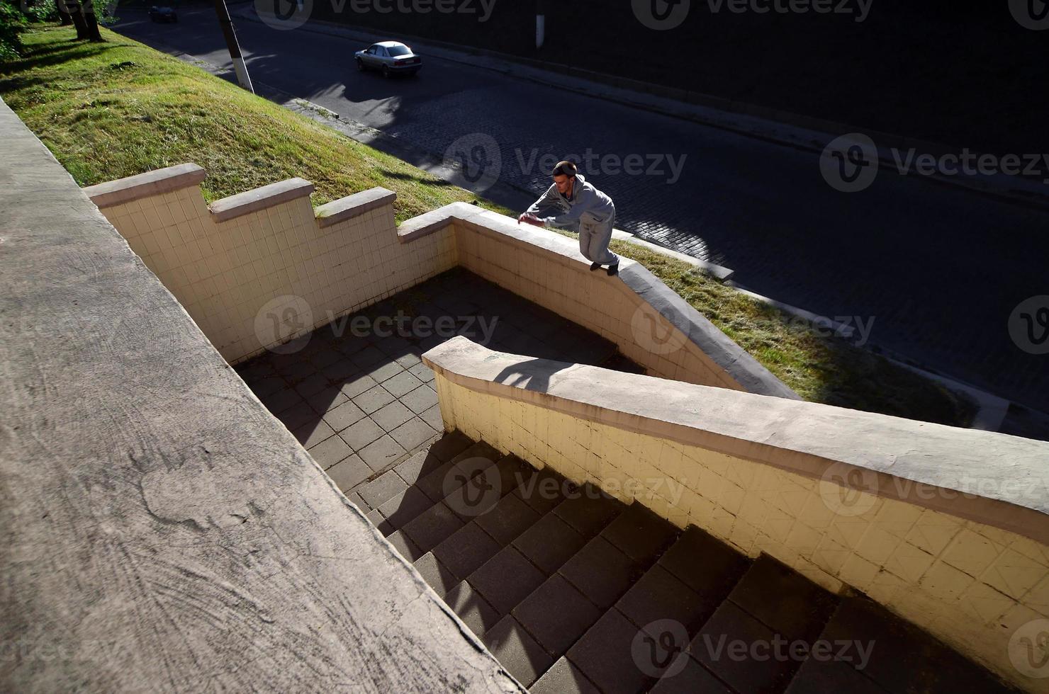 ein junger mann macht einen sprung durch den raum zwischen den betonbrüstungen. Der Athlet übt Parkour und trainiert unter Straßenbedingungen. das Konzept der sportlichen Subkulturen unter Jugendlichen foto