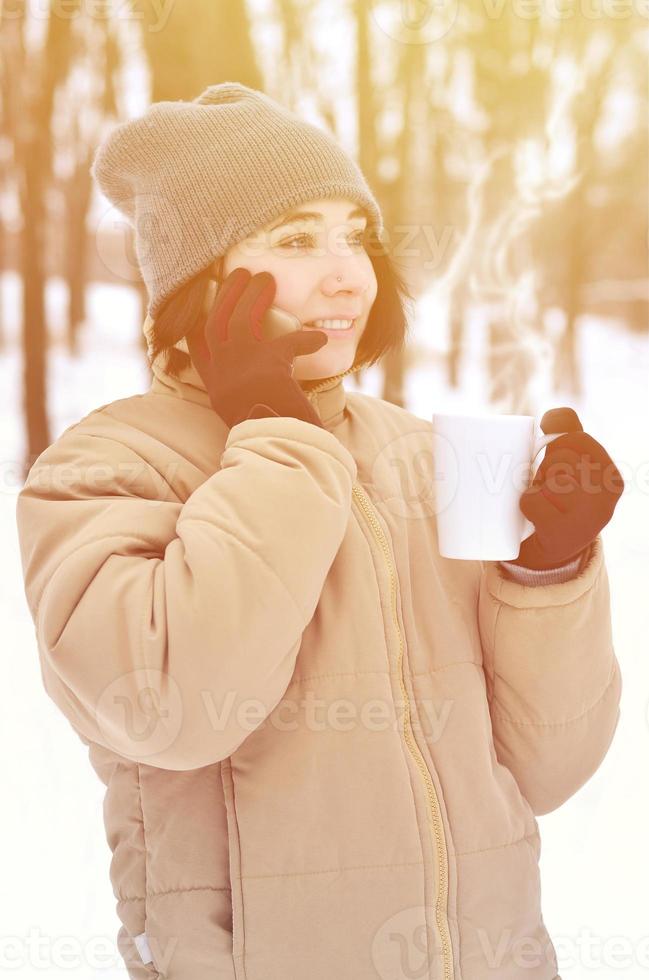 Winterporträt eines jungen Mädchens mit Smartphone und Kaffeetasse foto