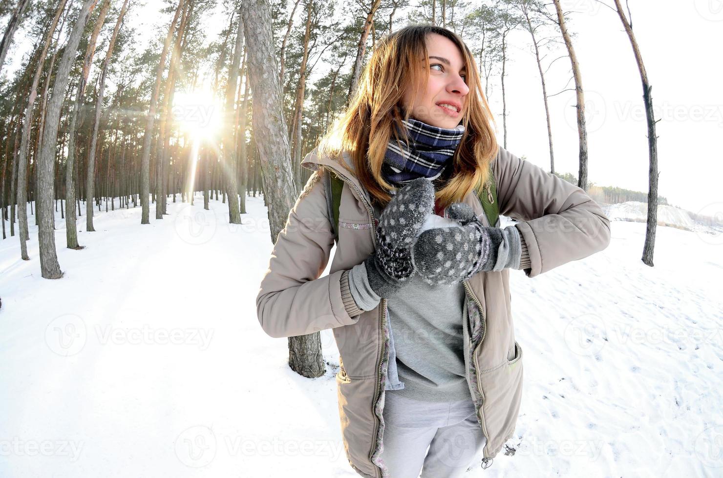 ein junges und fröhliches kaukasisches mädchen in einem braunen mantel formt im winter einen schneeball in einem schneebedeckten wald. Spiele mit Schnee im Freien. Fisheye-Foto foto