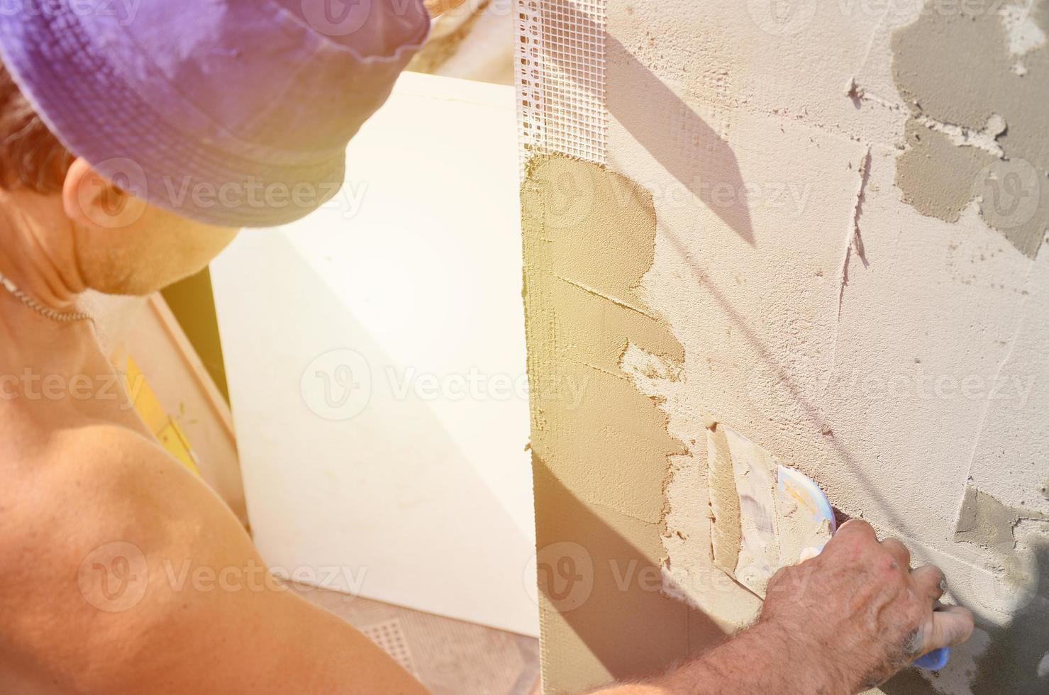 Fünfzig Jahre alter Arbeiter mit Wandputzwerkzeugen, die das Haus renovieren. Stuckateur renovieren Wände und Ecken mit Spachtel und Putz. Wandmaische Installation. Bauabschlussarbeiten foto