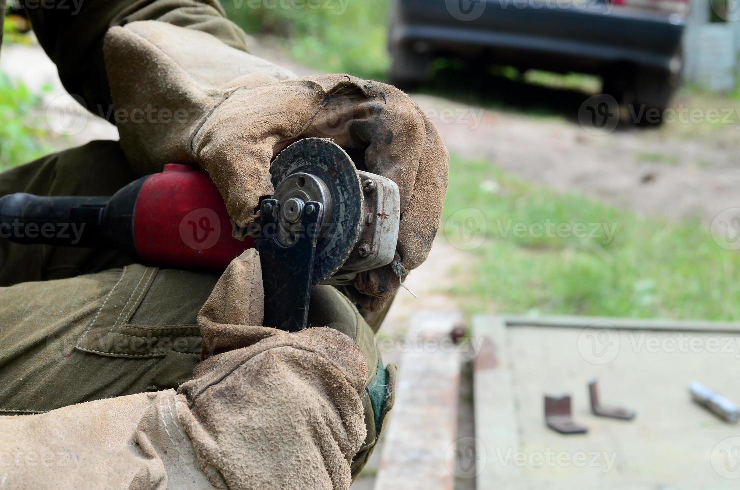 Elektrisches Radschleifen auf Stahlkonstruktion im Freien. alter arbeiter in schutzhandschuhen, der metalltür mit schleifer schneidet foto