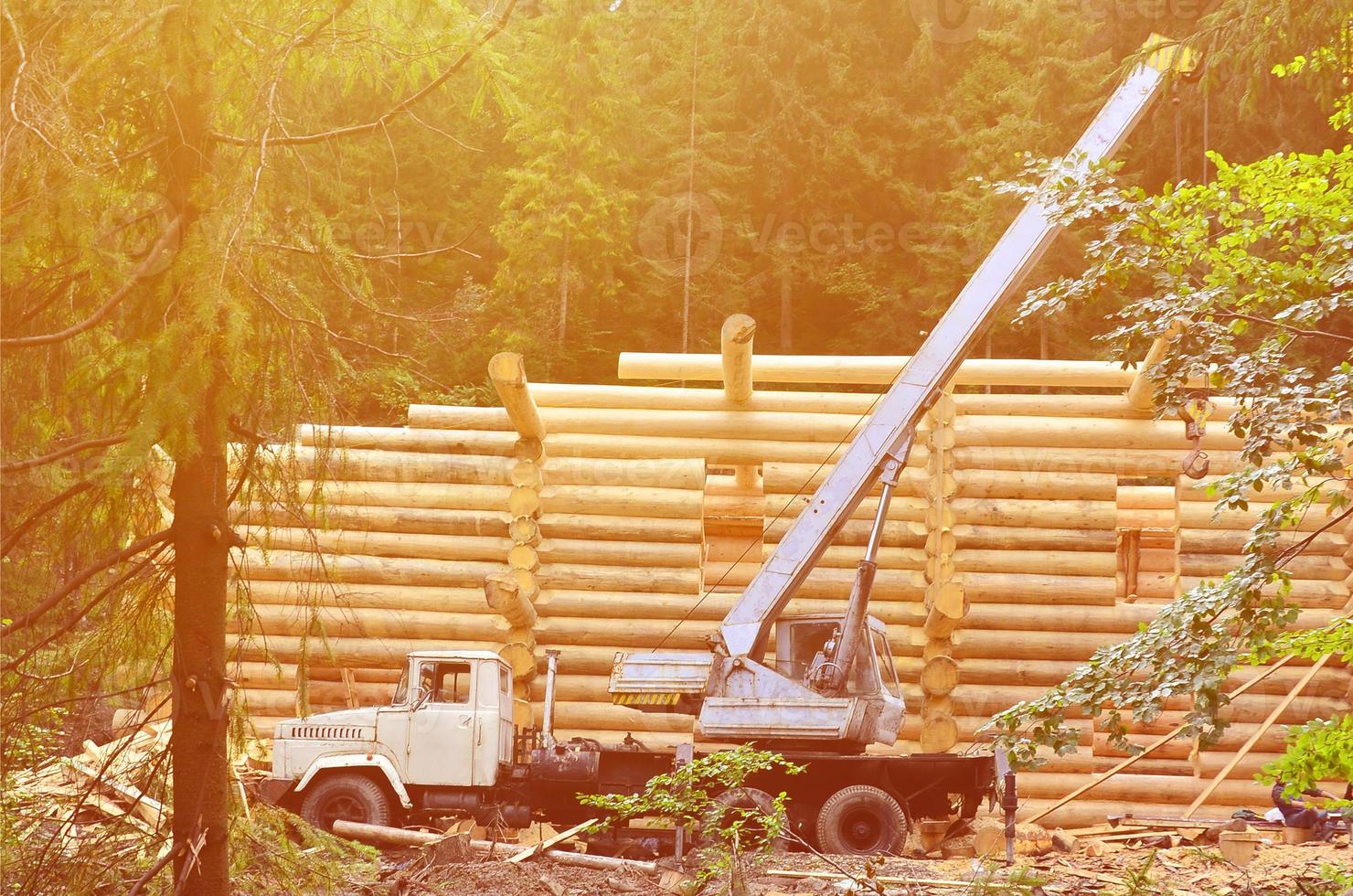 der Prozess des Baus eines Holzhauses aus Holzbalken mit zylindrischer Form. Kran in funktionstüchtigem Zustand foto