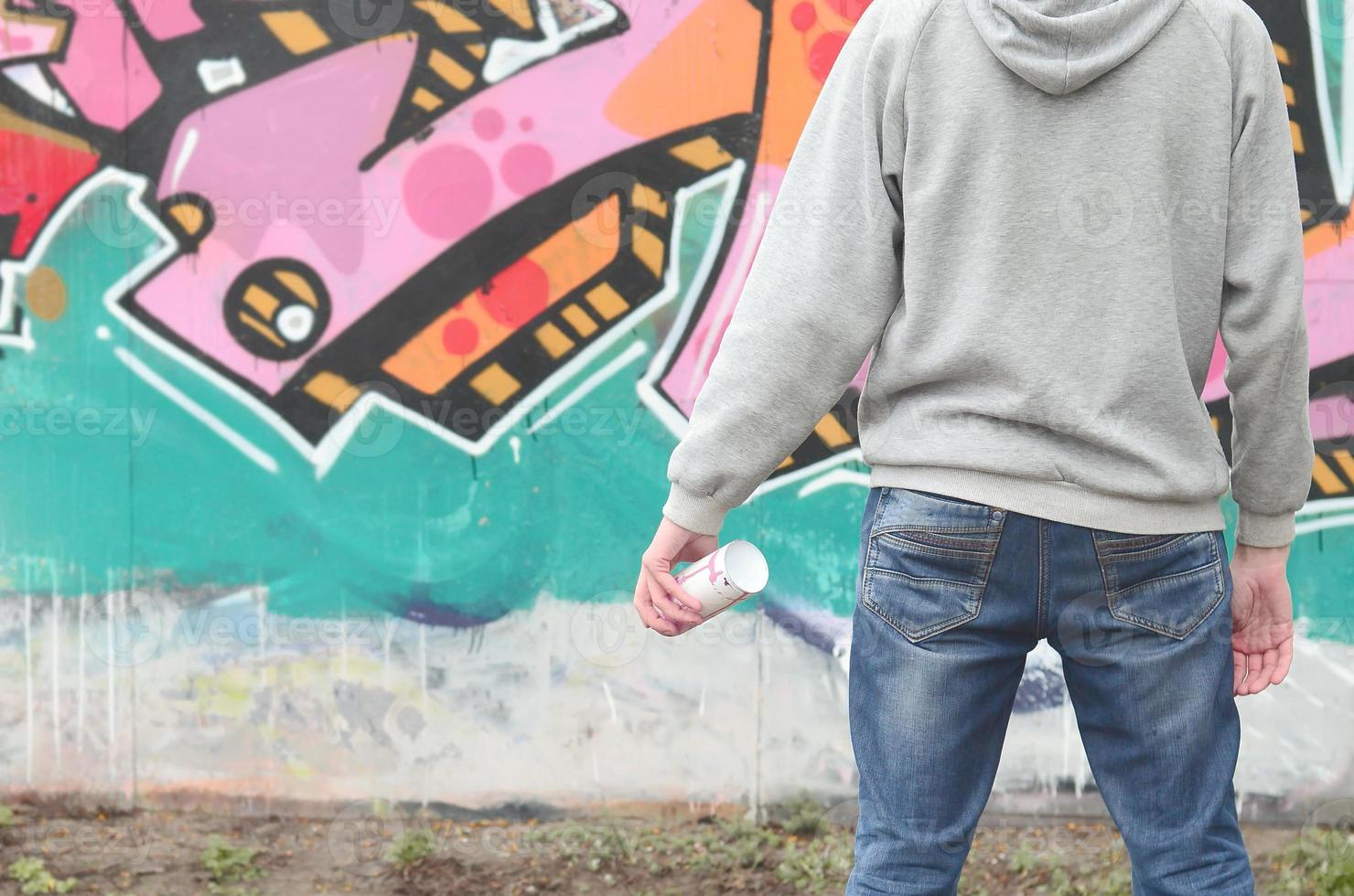 Ein junger Graffiti-Künstler in einem grauen Hoodie blickt mit auf die Wand foto