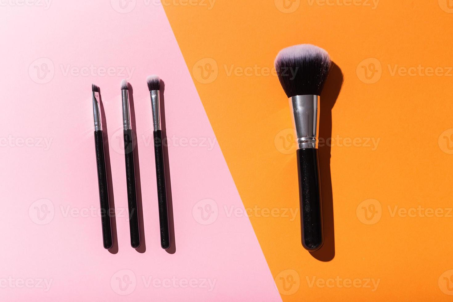 Verschiedene Make-up-Pinsel auf rosa und orangefarbenem Hintergrund, Ansicht von oben. kosmetik- und schönheitskonzept. foto