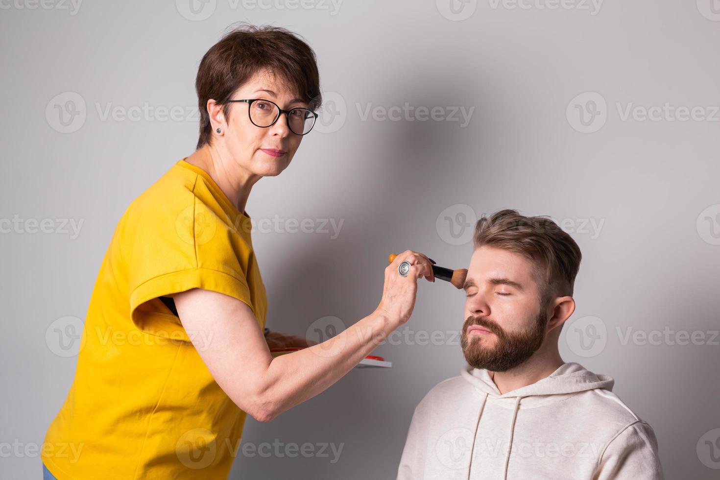 Professioneller Make-up-Künstler, der junge Männer im Studio schminkt foto