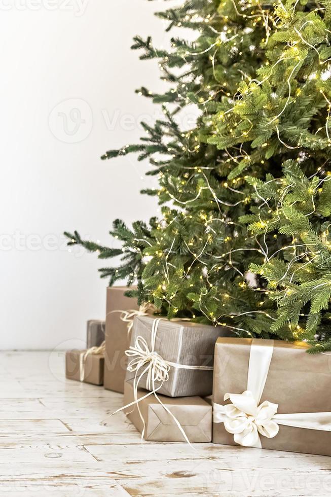 schöne geschenkboxen auf dem boden neben dem weihnachtsbaum im zimmer. weihnachts- und neujahrskonzept foto