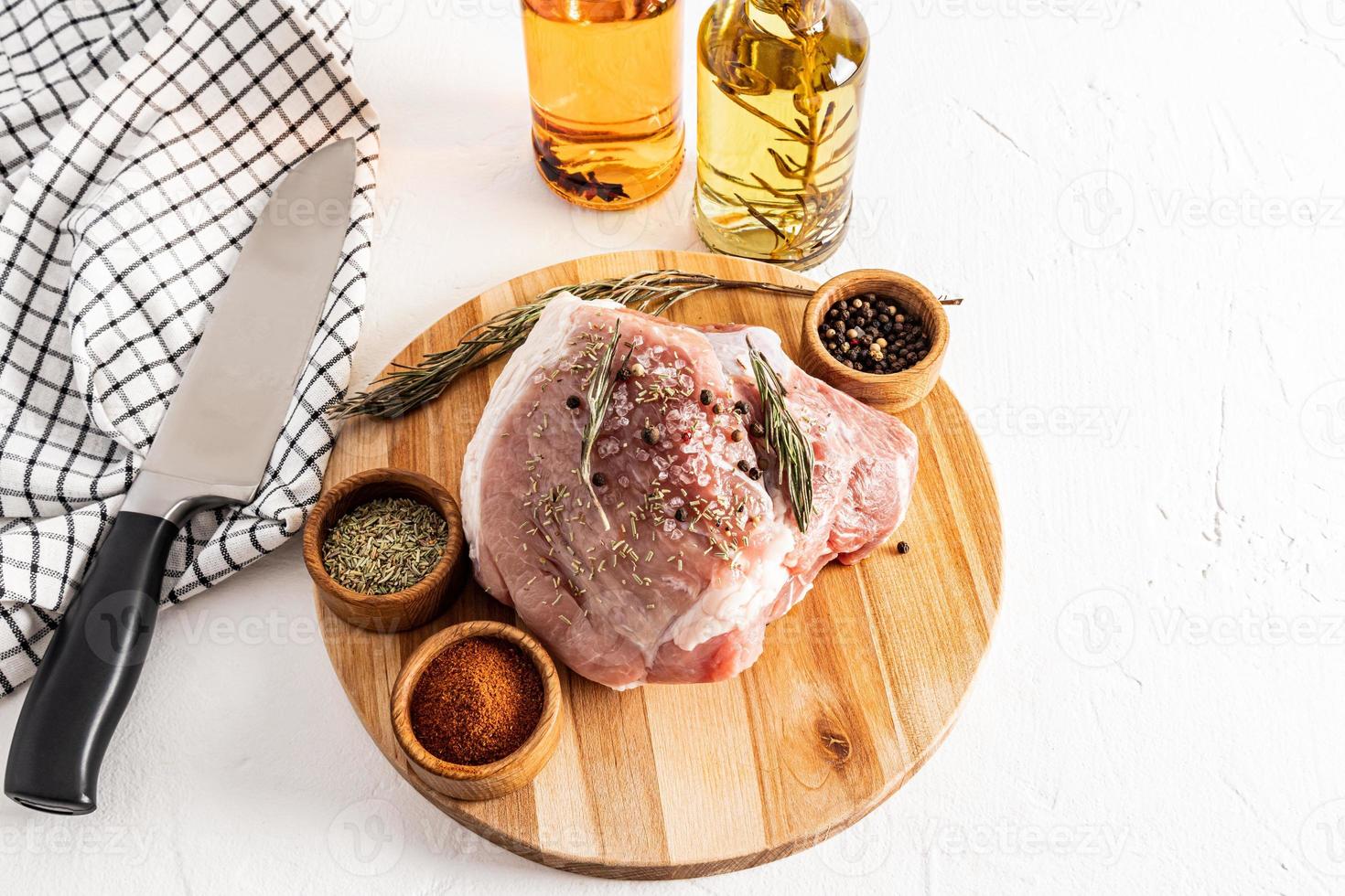 Ein großes Stück roher Schweineschinken auf einem runden Holzschneidebrett. Öl in Flaschen, Gewürze in Schalen zum Marinieren von Fleisch. weißer Hintergrund. foto
