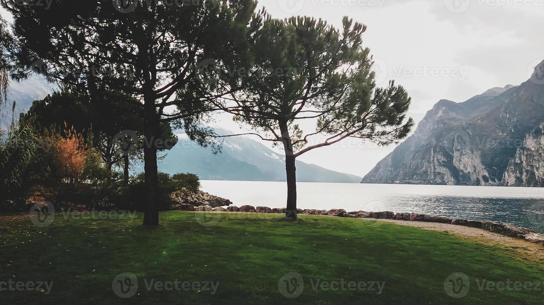 schöne aussicht auf einen bergsee im frühherbst, immergrüne kiefern, grünes gras an den ufern des erstaunlichen gardasees in italien foto