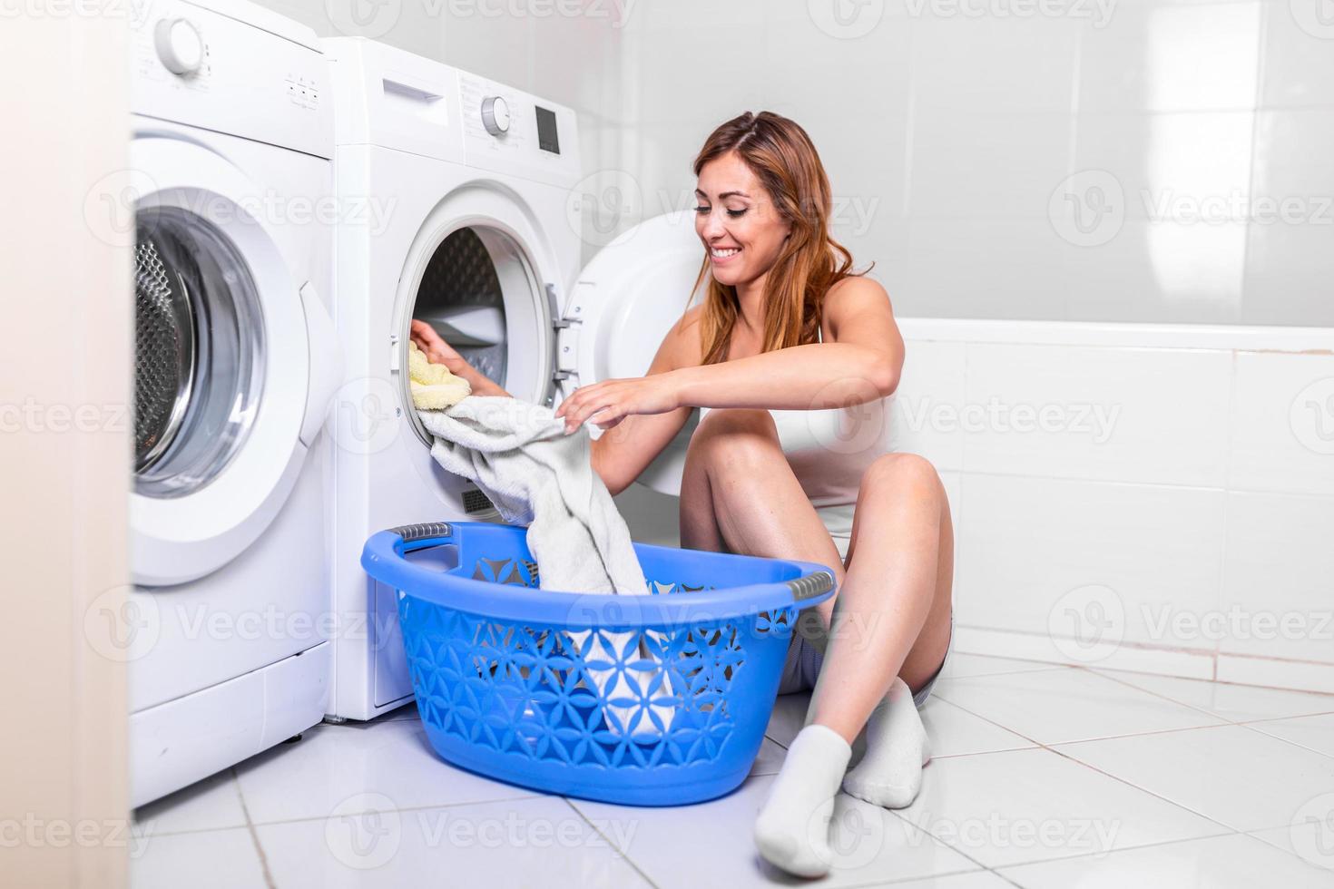 junge frau, die zu hause wäsche aus der waschmaschine nimmt. junge frau zu hause, macht hausarbeiten und hauswirtschaft, sammelt kleidung und kleider aus wäschetrockner, trockner foto