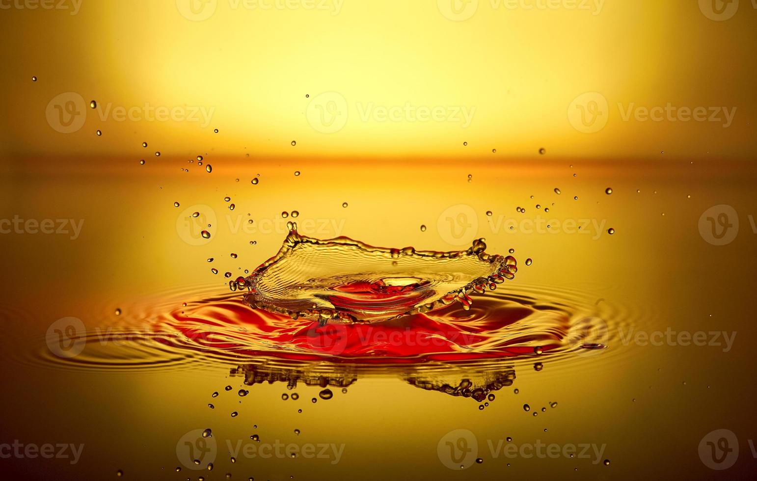 spritzer roter flüssigkeit mit reflexion und tropfen auf gelbem hintergrund foto