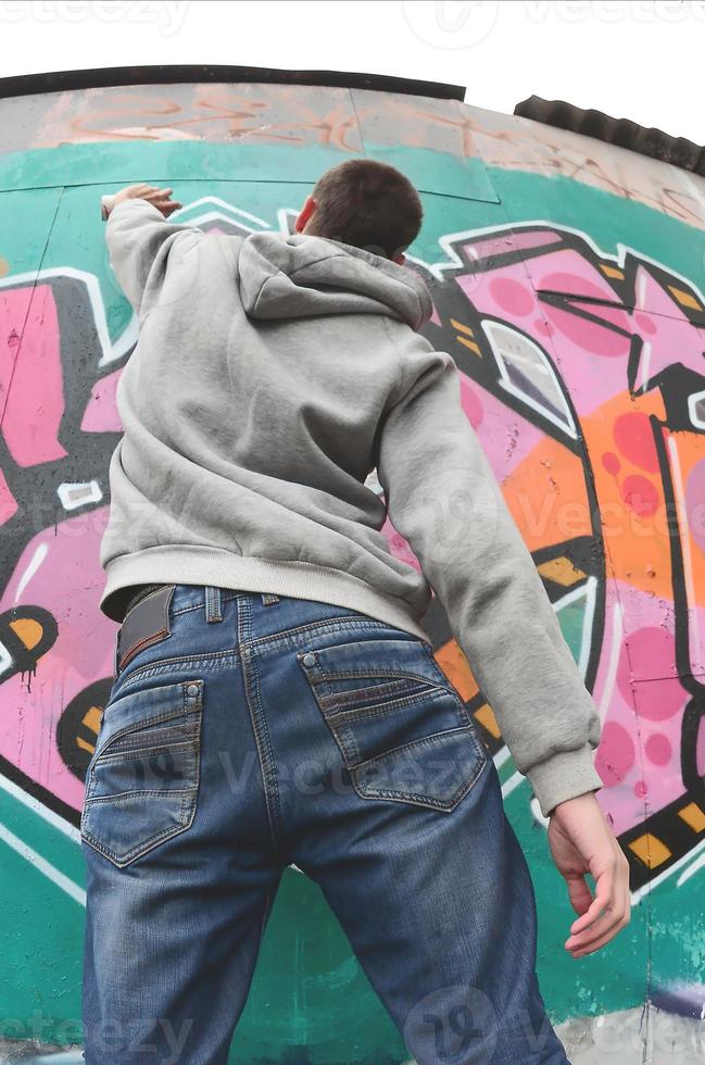 ein junger Mann in einem grauen Hoodie malt Graffiti in Pink und Grün c foto