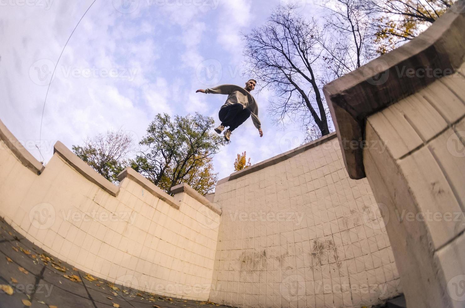 ein junger mann macht einen sprung durch den raum zwischen den betonbrüstungen. Der Athlet übt Parkour und trainiert unter Straßenbedingungen. das Konzept der sportlichen Subkulturen unter Jugendlichen foto