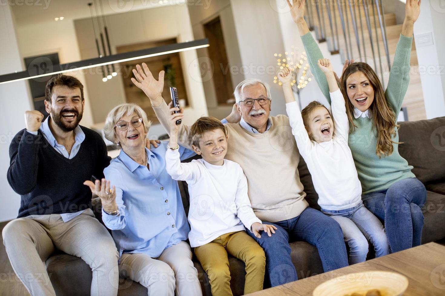 Familie mit mehreren Generationen, die einen Fußball im Fernsehen sieht und ein Tor feiert, sitzt auf der Couch im Wohnzimmer foto